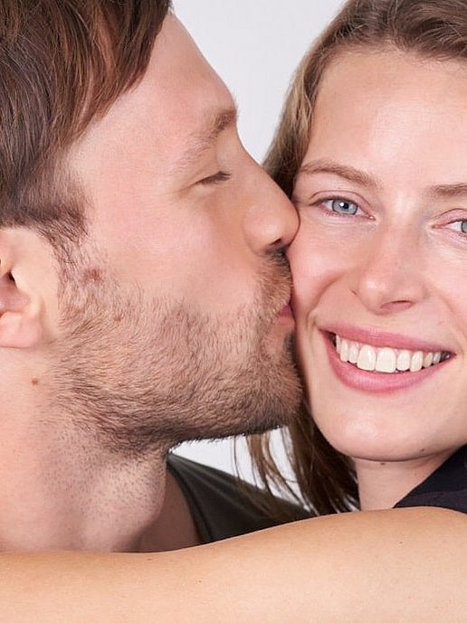 Man kust lachende vrouw bij een date op haar wang.