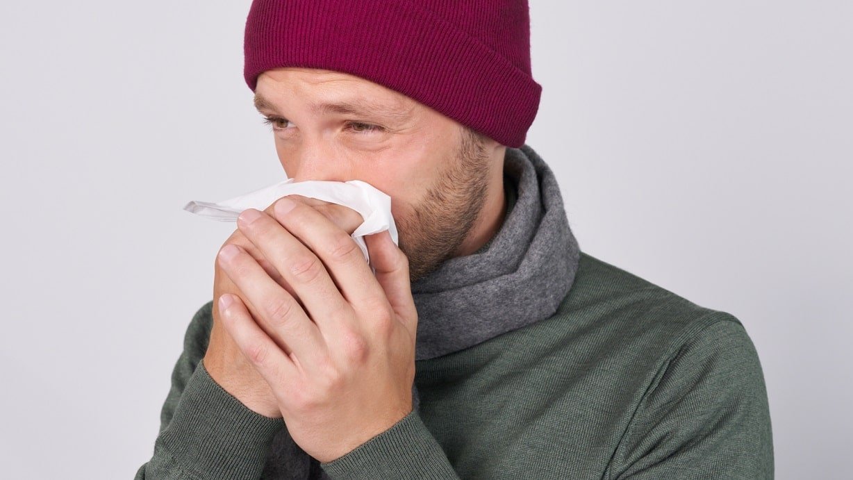 Erkälteter Mann schnäuzt sich die Nase.