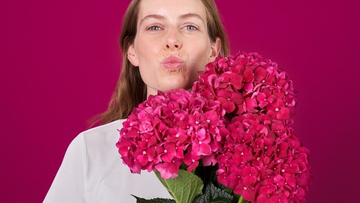 Une femme avec un bouquet de fleurs montre ses lèvres sans bouton de fièvre comme pour donner un baiser.