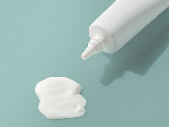 Eine weiße Tube gibt eine kleine Menge cremiger Lotion auf eine hellblaue Oberfläche ab.